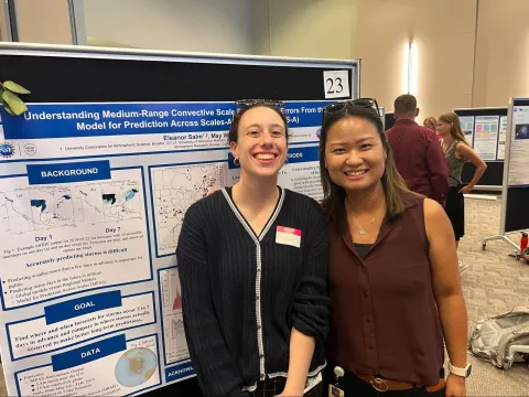 Two students pose in front of a poster.